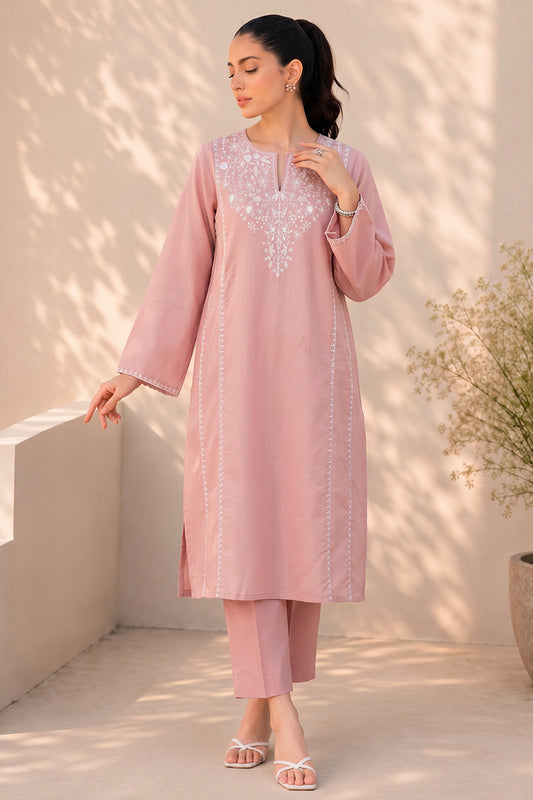 A woman modeling a dusty pink traditional kurta set with matching trousers, featuring white embroidered detailing around the neckline and down the front, set against a sunlit beige wall with leaf shadows.