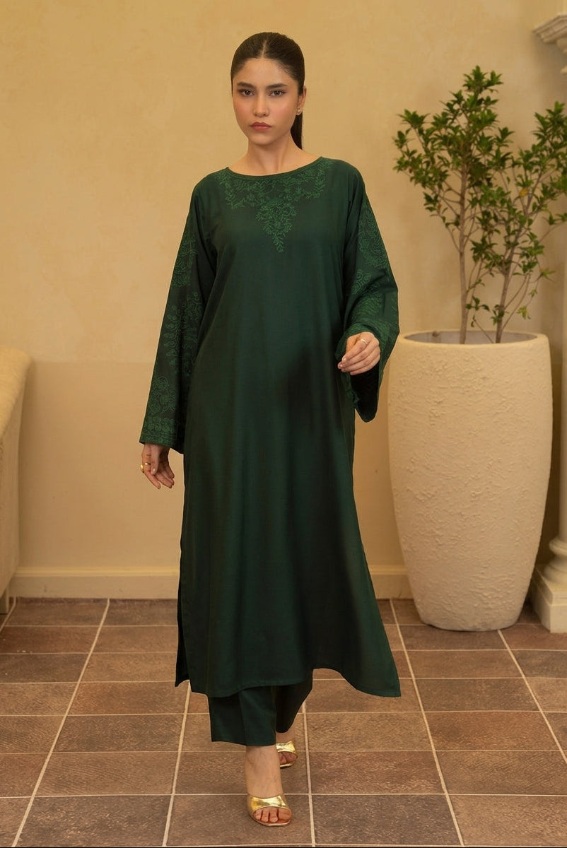 A woman modeling a dark green long kurta with matching pants in an indoor setting with beige walls, tiled flooring, and a large potted plant.