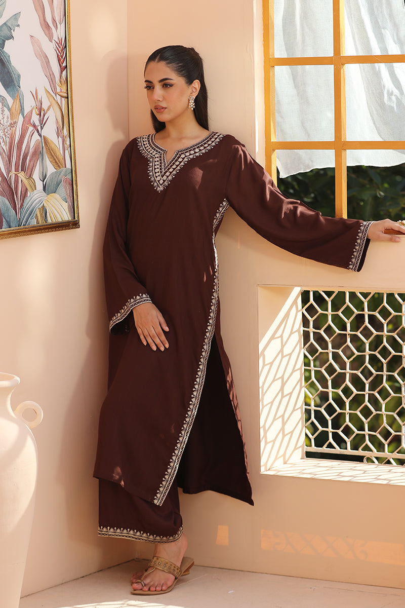 A woman models a dark brown long kurta with silver embroidered details on the neckline, hem, and cuffs, paired with matching wide-leg trousers, in a warm-toned indoor setting.