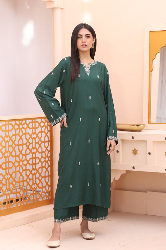 A woman modeling a dark green long kurta with silver embroidery and matching green pants in a warm-toned indoor setting.