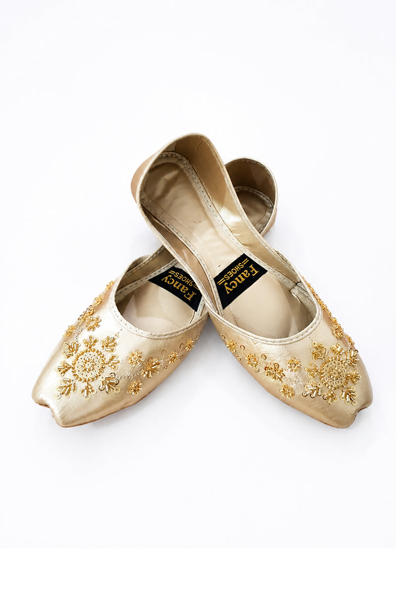 A pair of gold satin flat shoes with intricate gold floral embroidery, displayed on a clean white background. The shoes feature a pointed toe and a black brand label inside.