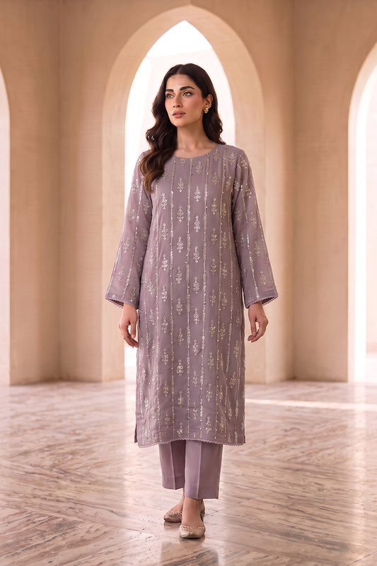 A woman modeling a lavender-purple kurta with vertical metallic gold embroidery, paired with matching pants, in a grand arched hall with beige walls and marble floors.