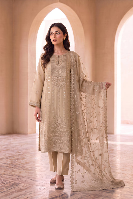 A woman models a traditional beige three-piece salwar kameez suit with intricate embroidery, featuring a long kurta, matching trousers, and a sheer embroidered dupatta, set against an elegant arched corridor.