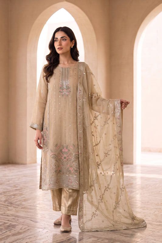 A woman models a traditional beige three-piece salwar kameez suit with intricate embroidery and a matching sheer dupatta, set against a warm architectural background with arched windows.