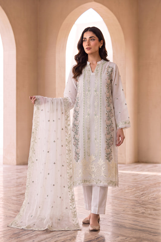A woman models a traditional white three-piece salwar kameez suit with intricate silver and gold embroidery, holding up the matching dupatta in a grand arched hall.